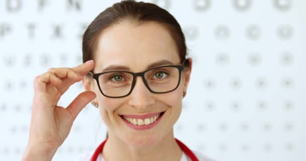 Γυναίκα οφθαλμίατρος γιατρός απογειώνει τα γυαλιά στο παρασκήνιο του πίνακα της όρασης 4k ταινία αργή κίνηση — Αρχείο Βίντεο