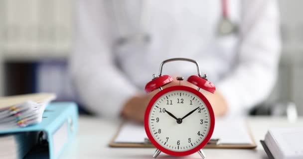 Červený budík pro deset hodin stojí na stole lékaře — Stock video