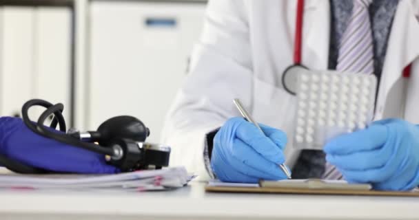 Lekarz trzymający blister z tabletkami w rękach i wypisujący receptę w klinice 4k film slow motion — Wideo stockowe