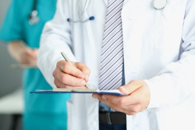 Doktor elinde bir klasör tutuyor ve yazıyor.