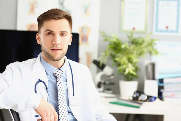 Hezký mužský doktor sedí u stolu na klinice — Stock fotografie