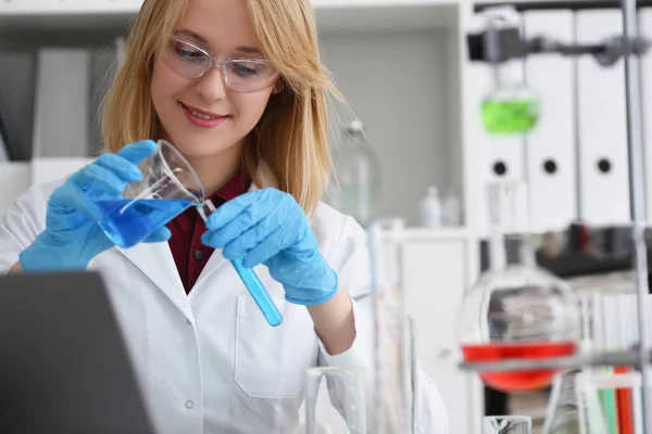 Een vrouw in een laboratorium giet blauwe vloeistof in een testbad — Stockfoto