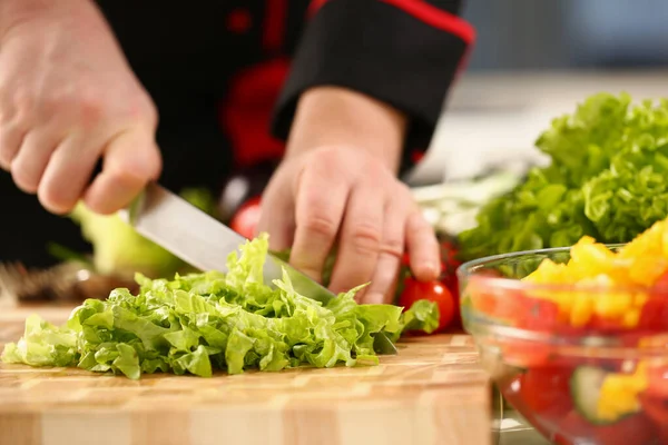 Um chef macho corta uma salada verde com uma faca — Fotografia de Stock