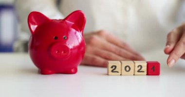 İş kadını 2021 'den 2022' ye kadar sayıları küplere çeviriyor. Yanında kırmızı domuz kumbarası var.