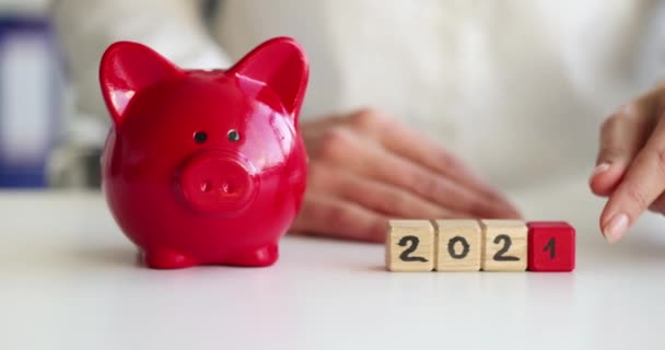 Unternehmerin dreht Zahlen auf Würfel von 2021 bis 2022, daneben steht rotes Sparschwein — Stockvideo