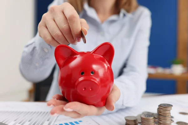 Business woman throwing coins into piggy bank at table with graphs closeup — Stock Photo, Image