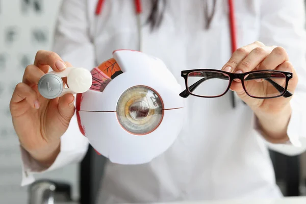 Ophthalmologist doctor holding eyeglasses and lenses near artificial model of eye closeup — Stock Photo, Image