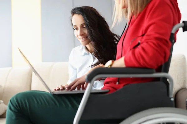 Кращі друзі проводять час разом, дивлячись фільм на ноутбуці, жінка в інвалідному візку тримає пристрій на колінах — стокове фото