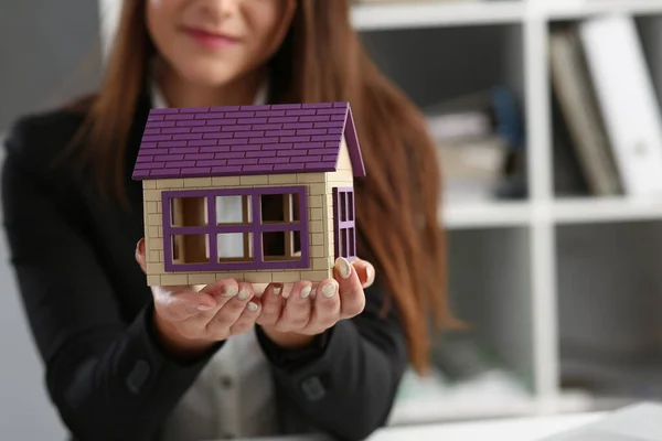 Mulher no escritório segurar casa de brinquedo em miniatura na mão símbolo de imóveis — Fotografia de Stock