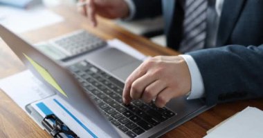 İşadamı ofis masasında otururken dizüstü bilgisayar ve hesap makinesi kullanır.