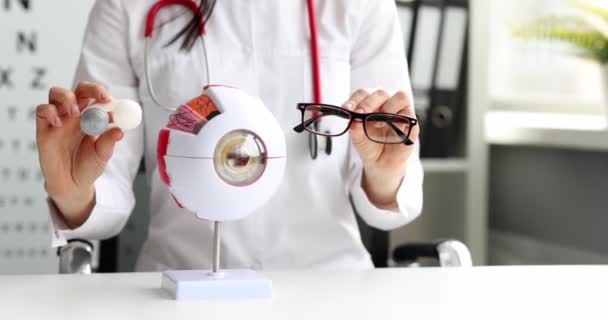 Médecin ophtalmologiste tient des lunettes et des lentilles de contact sur fond de maquette de l'œil humain — Video