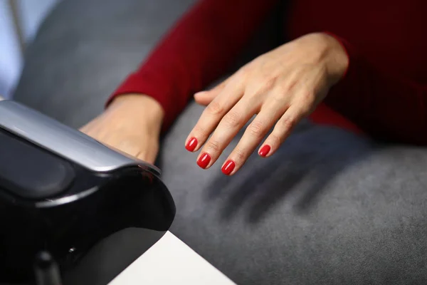 Женщина клиент положить руку со свежими красными ногтями под лампой, чтобы высушить его — стоковое фото