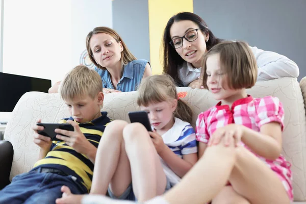 Los niños juegan juegos en línea en los teléfonos móviles y las mamás controlan verlos — Foto de Stock