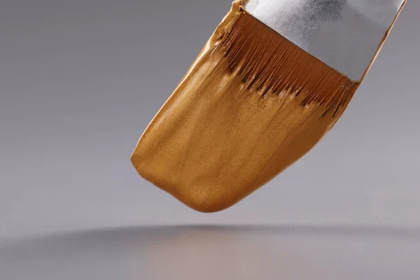 Fechar a escova com tinta dourada sobre fundo cinza — Fotografia de Stock