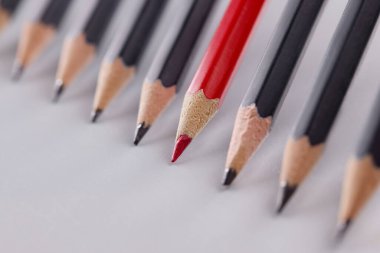 Gri arkaplandaki birbirinin aynısı siyah kalemlerden göze çarpan kırmızı kalem.