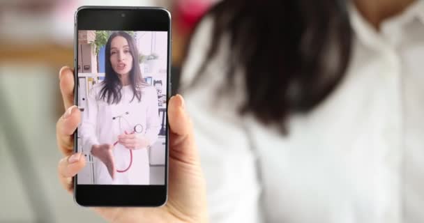 Mujer sosteniendo el teléfono móvil en sus manos donde el médico está hablando en video enlace película 4k — Vídeos de Stock