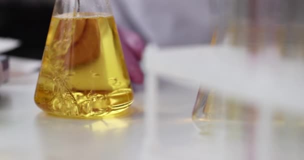O líquido é adicionado frasco com líquido oleoso amarelo que realiza a experiência química — Vídeo de Stock