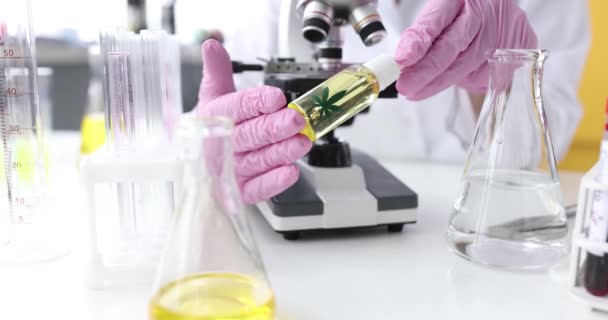 Científico en guantes sostiene botella de aceite de marihuana en laboratorio — Vídeo de stock