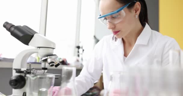 젊은 여성 과학자가 식탁을 닦고 냅킨으로 현미경을 사용하다 — 비디오