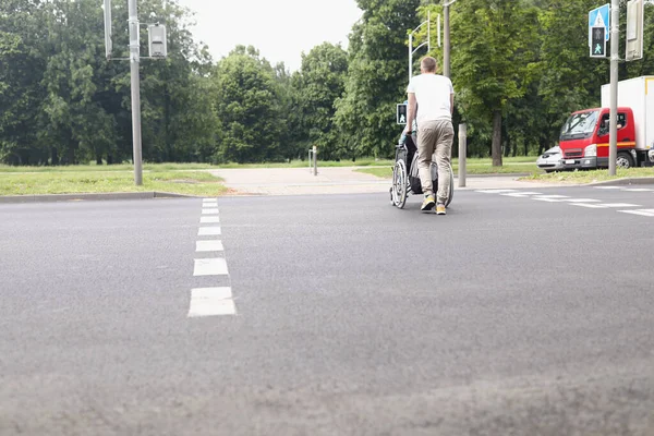 Hombre conducir mujer en silla de ruedas a través de la calle en el cruce peatonal — Foto de Stock