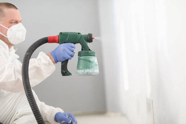 Worker using spray gun for coloring wall in white. Effective and fast way to paint wall