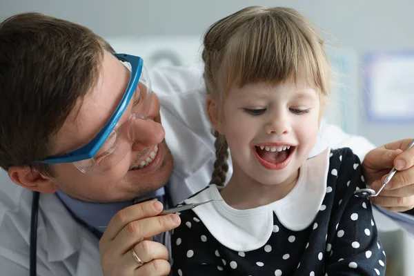 Man barnläkare kontrollera små flickor hälsotillstånd med hjälp av speciella verktyg för munnen — Stockfoto