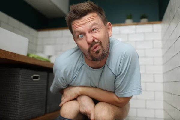 Людина з смішним виразом обличчя на сидінні в туалеті, задовольняє природну потребу — стокове фото