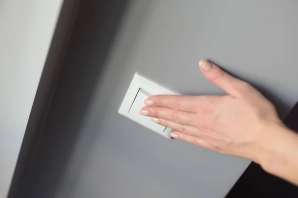 Uma mão de mulher aperta um interruptor branco em uma parede cinza — Fotografia de Stock