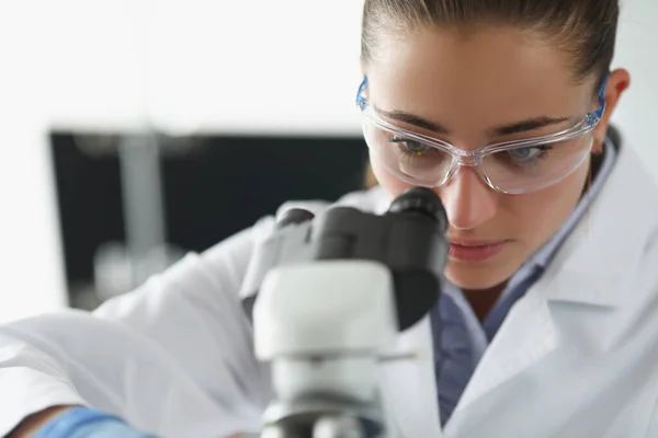 Vrouwelijke chemicus onderzoekt monster onder microscoop apparatuur in het lab — Stockfoto