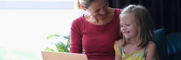 Sonriente mamá y su hija sentado en el sofá y mirando a la computadora portátil — Foto de Stock