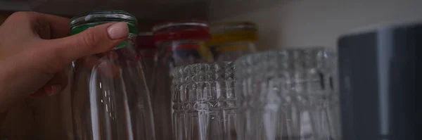 Žena ruka vytáhne skleněný šálek ze skříňky v kuchyni — Stock fotografie