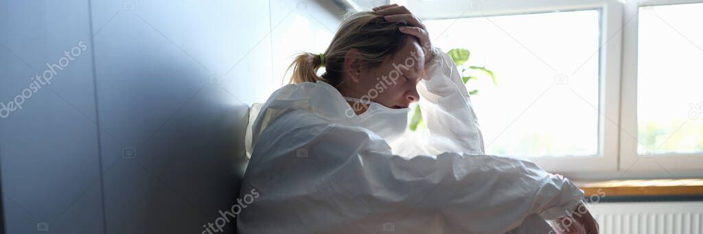 Tired female doctor in medical protective suit and mask in hands after work in clinic