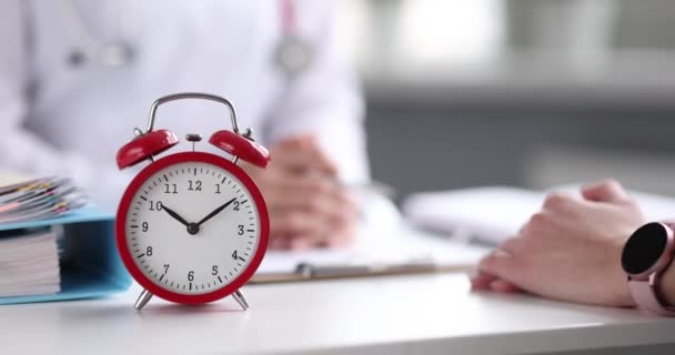 Médico realiza consulta com paciente em primeiro plano com despertador vermelho — Vídeo de Stock
