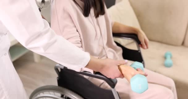Врач помогает пациенту в инвалидной коляске делать упражнения с гантелями — стоковое видео