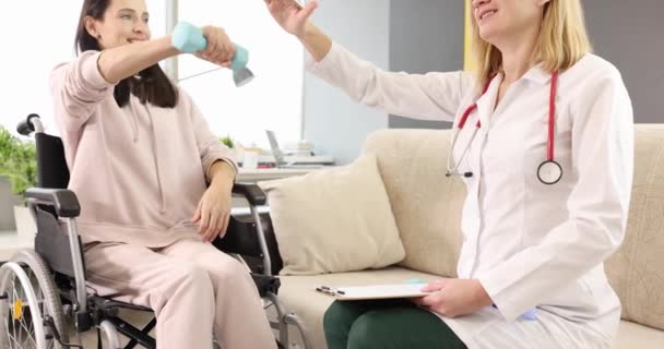 Реабилитационный врач помогает женщине в инвалидном кресле делать упражнения с гантелями — стоковое видео