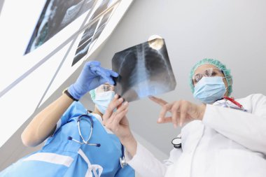 Tıbbi önlüklü doktorlar klinikteki hastanın akciğerlerinin röntgenini inceliyor.