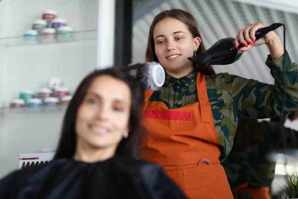 お客様の髪型で治療のためのヘアドライヤーを使用して陽気美容師 — ストック写真