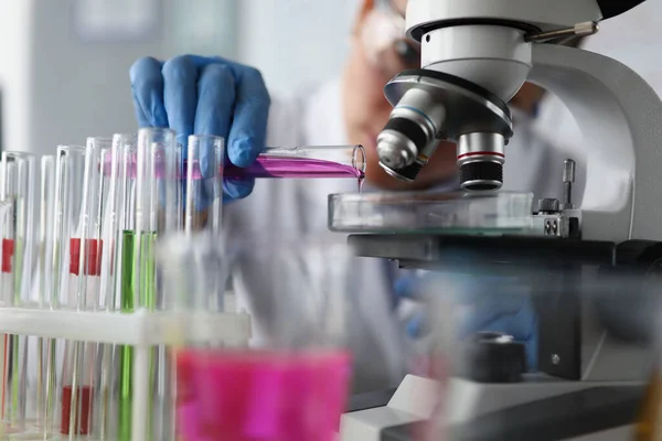 실험실에서 현미경으로 유리 용기에 분홍색 샘플 액을 부어 주는 여성 과학자 — 스톡 사진