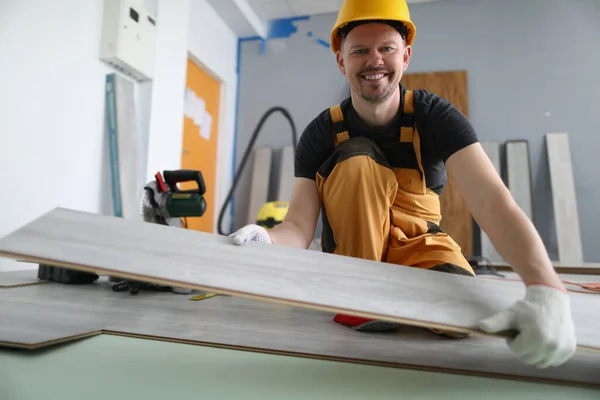 Gekwalificeerde timmerman glimlach en zet houten plank op de vloer — Stockfoto