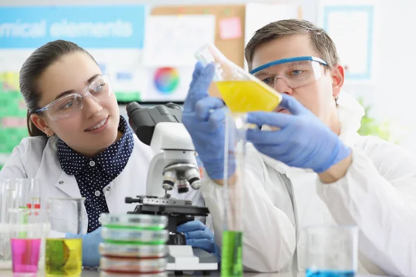 Trabalhadores de laboratório homem e mulher examinam líquido amarelo em frasco. — Fotografia de Stock