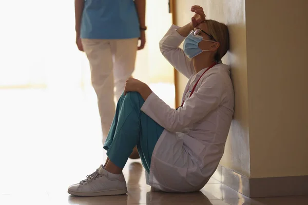 Femmina chirurgo espirare dopo lunga operazione seduto in corridoio clinica sul pavimento — Foto Stock
