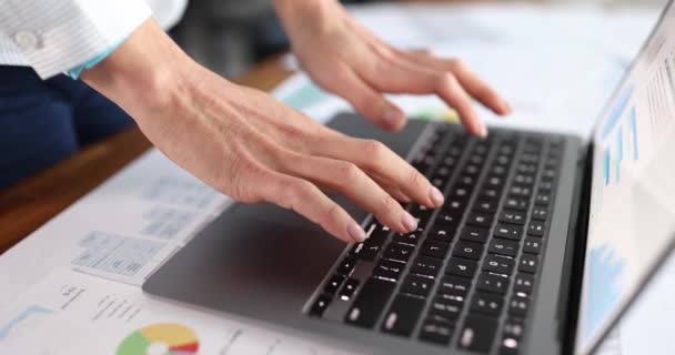 Vrouwelijke handen typen op laptop toetsenbord onder documenten met grafieken closeup 4k film slow motion — Stockvideo