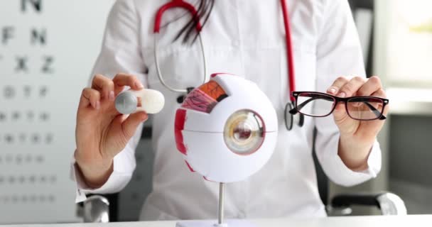 Doctor oftalmólogo sosteniendo contenedor con lentes de contacto y gafas delante del modelo de ojo humano artificial 4k película cámara lenta — Vídeos de Stock