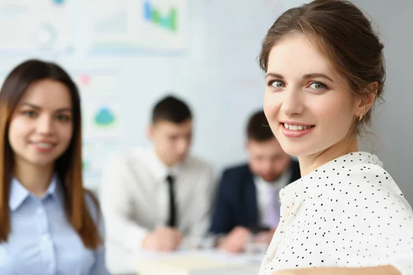 Mujer inteligente sentada en una gran oficina moderna con colegas y sonrisa ante la cámara —  Fotos de Stock