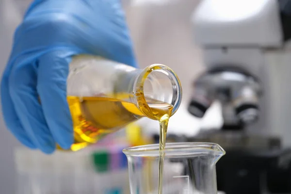 Een hand in een handschoen giet een gele vloeistof in het laboratorium — Stockfoto