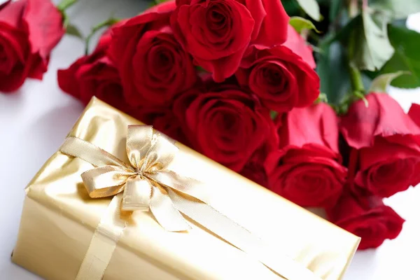 Ajándék aranyba csomagolva és egy csokor vörös rózsával. — Stock Fotó
