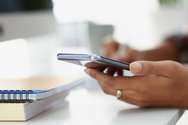 Ofiste spiral defter ile masada otururken modern akıllı telefon kullanan kadın.