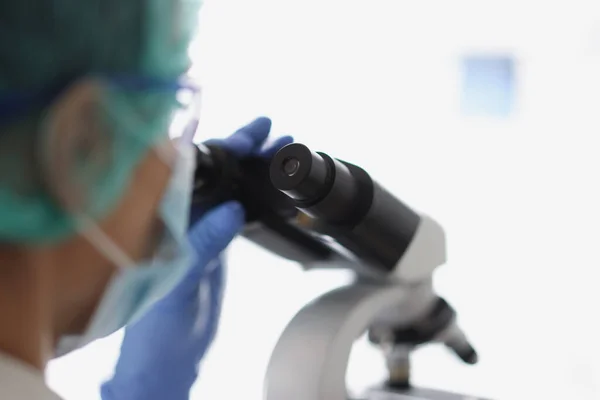 Mulher química em luva protetora azul olhar para o microscópio no laboratório de química — Fotografia de Stock