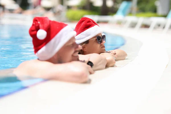 Чоловік і жінки в капелюхах Сантаклав відпочивають у басейні — стокове фото