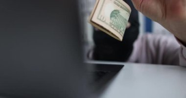 Siyah maskeli siber suçlu dolarları kancada tutuyor ve bilgisayara bakıyor.